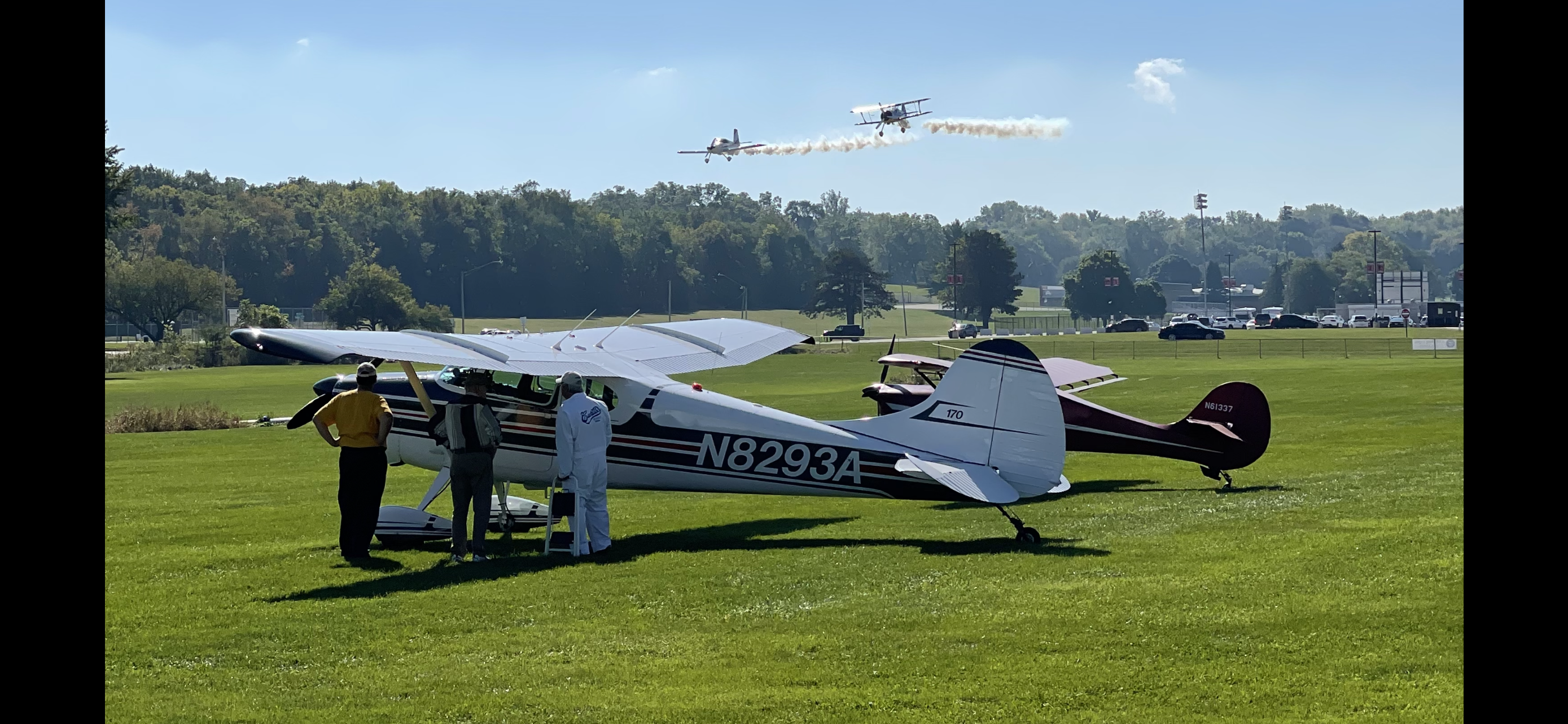 Aircraft and chapter members gathered on the grass with planes flying in the distance