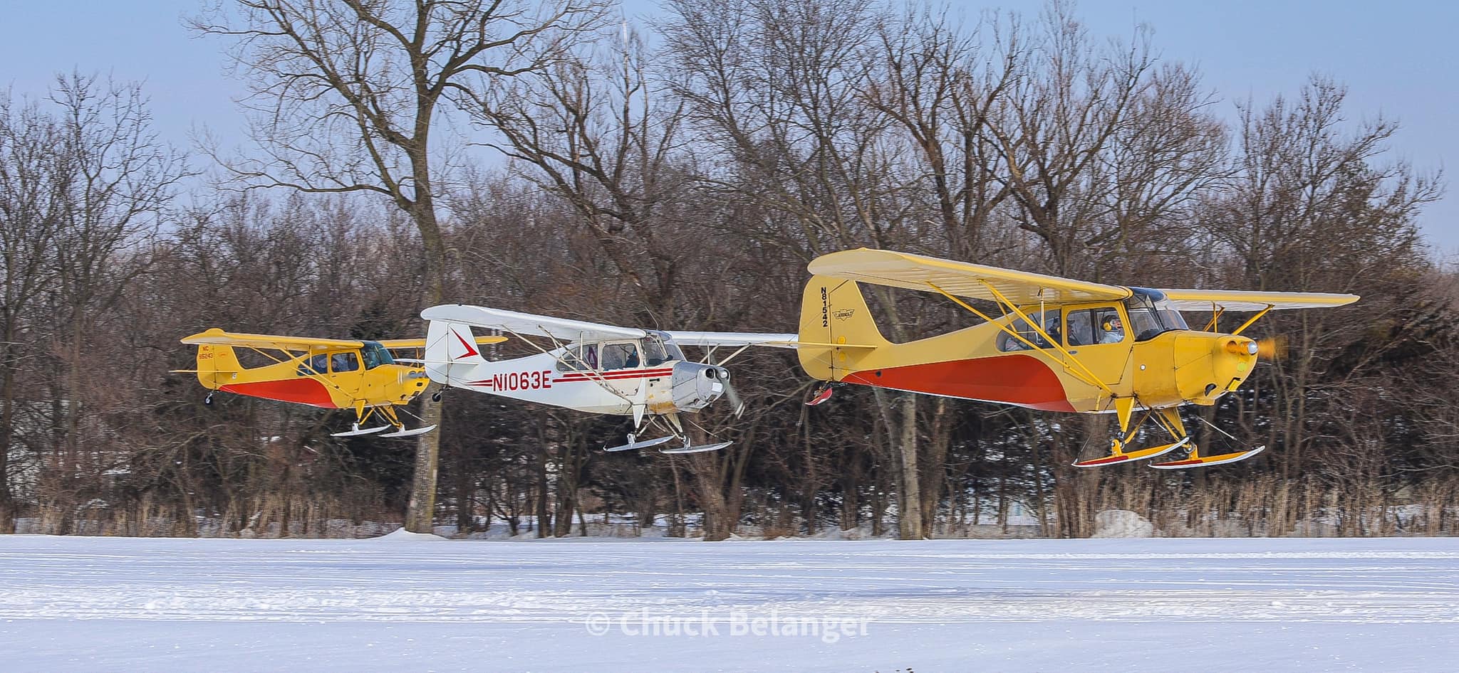 Three aircraft flying in formation over a snowy field